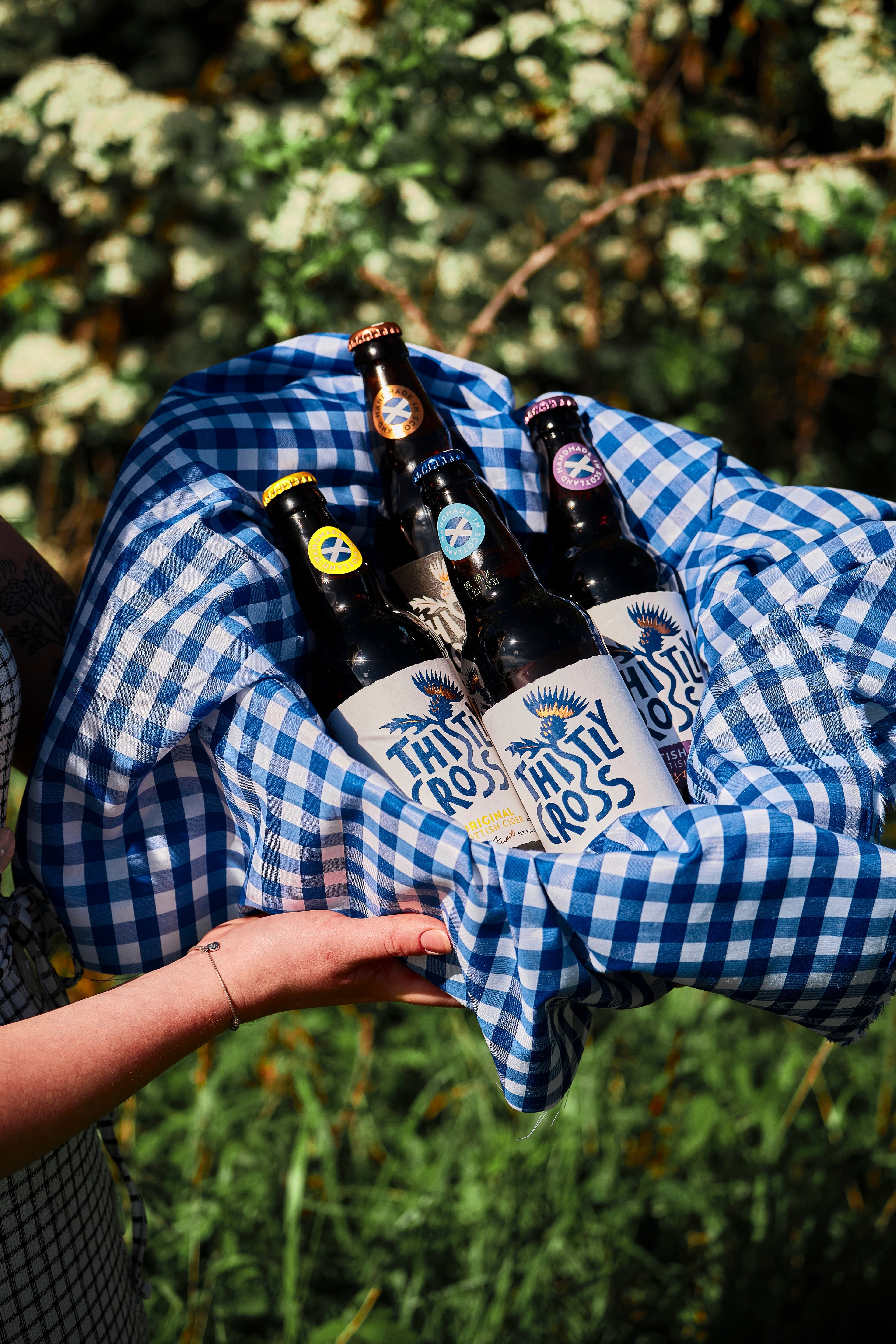 A person holding a basket of thistly cross cider bottles